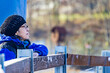© Emile - Close-up of a mature woman with glasses, winter clothes and black hat observing and very pensive next to a wooden fence with a blurred background. Space for text