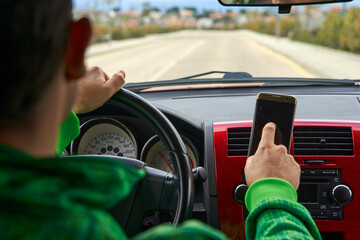 Male driver touching a smartphone screen on the dashboard while he are driving.