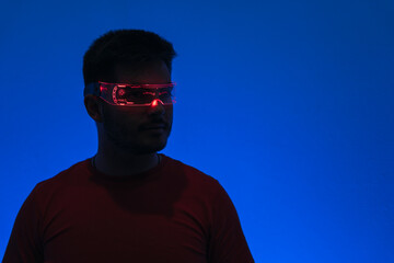 Silueta de un chico con gafas futuristas de luz led en fondo azul.