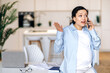 Outraged pregnant busy woman. Stressed irritated mixed race pregnant woman, business lady or office coworker, stylishly dressed, standing near the table, indignantly talking on the phone