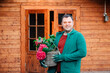 A young horticulturist holds a red hydrangea and smiles. Man is standing in the garden with a wooden garden shed in the background. Gardening with fun. Life in the countryside	