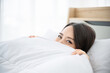 © Monster Ztudio - Young asian woman waking up in the morning on bed. She hiding body under the blanket and showing her eye out the blanket feeling happy