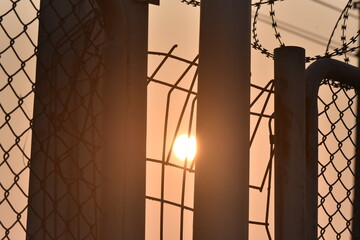 Sunlight falls through a barbed wire fence on the wall, shadows.