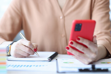 Woman writing in notebook and holding mobile phone in their hands closeup