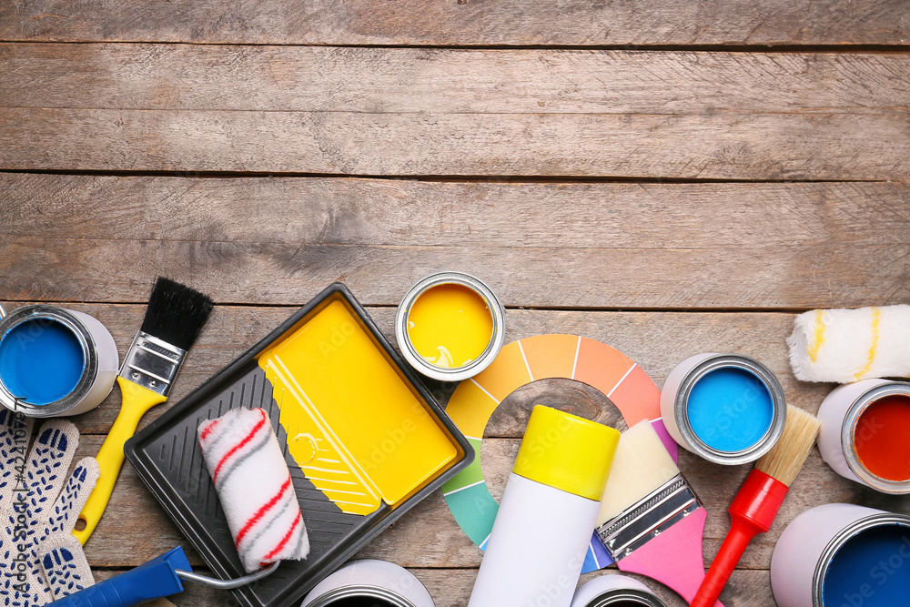 Cans of paints and tools on wooden background