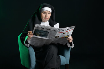 Wall Mural - Senior nun with newspaper and cigar sitting in armchair on dark background