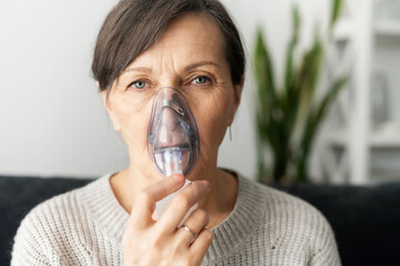 headshot of sick senior lady using oxygen mask at home, a mature woman has labored breathing, treatm