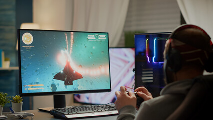 Gamer player with headphones and joypad performing space shooter video game during gaming championship. Online streaming cyber performing at virtual esports tournament using wireless joystick