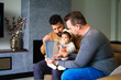 gay couple and their daughter sitting on a sofa reading a story to their little girl.
