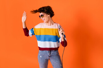 Photo of attractive carefree person arm hold mic look empty space palm wave isolated on orange color background