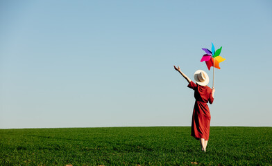 Woman in a red dress with pinwheel on country green wheat field in spring