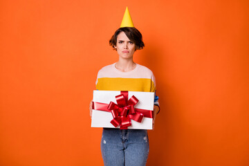 Poster - Portrait of attractive offended gloomy girl holding in hands gift dislike isolated over bright orange color background