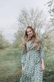 Fototapeta Las - beautiful girl with brown hair in a green dress in a blooming apple orchard with white flowers