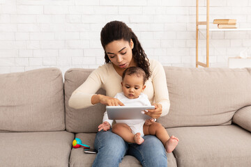 Wall Mural - Black Mother With Baby Using Tablet Computer Watching Cartoons Indoors