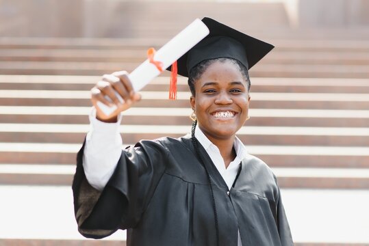 Young female african american student with diploma poses outdoors.