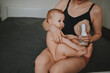© Алина Троева - Young mother with newborn cute infant naked baby boy, holding him on arms, using breast pump hugging and breastfeeds with breast milk. Healthy child, concept of hospital and happy motherhood. Nursery.