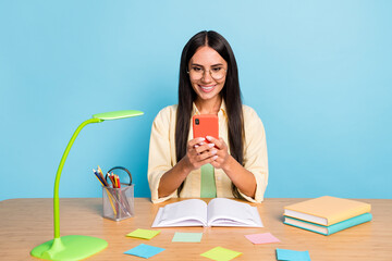 Poster - Portrait of pretty cheerful girl sitting behind desk typing post comment have good mood isolated on blue color background