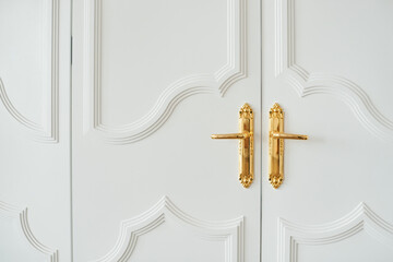 Close-up of white baroque doors with classic golden handles and ornaments. Beauty in details..Beautiful entrance to an expensive apartment. Copy space.