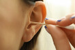 © Atlas - Woman cleans her ears with a cotton swab, close up