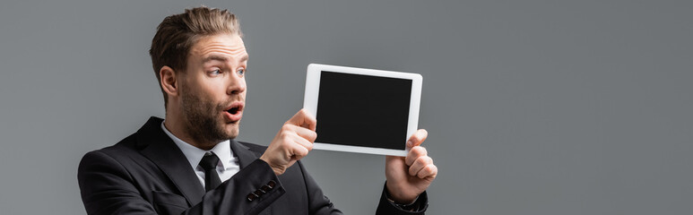 Wall Mural - astonished manager holding digital tablet with blank screen isolated on grey, banner