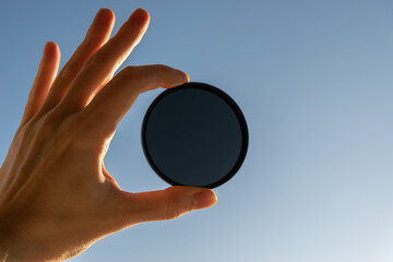 Hand hold ND-filter over blue sky background.