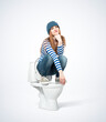 Young girl in casual clothes and hat squats on the toilet, on light background.