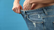 © Tatsiana - Cropped view of woman in big jeans on blue background, weight loss concept.
