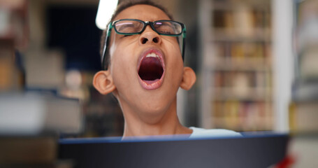 Poster - portrait of sleepy hard working schoolboy sitting at library and yawning using laptop