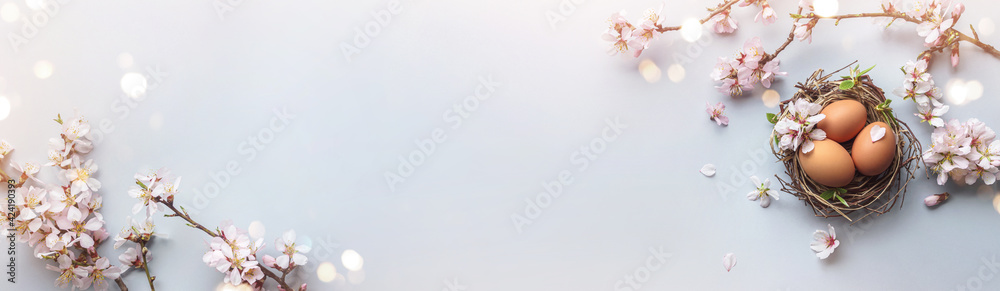 Easter eggs in nest and pink flowering sakura branches on light blue background. Happy Easter holiday, top view, flat lay - obrazy, fototapety, plakaty 