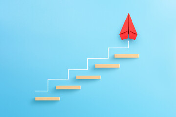 wooden block stacking as step stair with red paper plane on blue background, ladder of success in bu