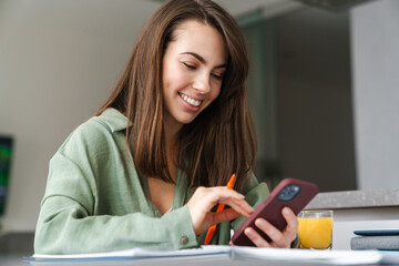 Young smiling woman using mobile phone while working with paper