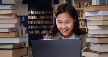 Canvas Print - Asian schoolgirl studying on laptop and smiling sitting in school library