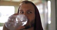 Young Adult Man With Hooded Sweatshirt Drinking Water Resting During Fitness