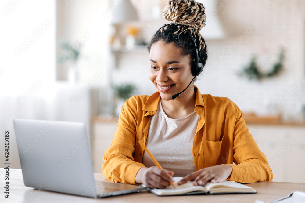 Concentrated confident friendly african american girl in headset, call center operator, manager, agent of support service, conducts online consultation, video briefing, taking notes, smiling friendly - obrazy, fototapety, plakaty 