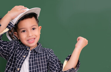 Asian little boy wear white engineer hat on blackboard.