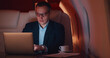 © nimito - Successful businessman in glasses working on laptop sitting in chair of private jet.