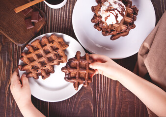 Homemade chocolate waffles with ice cream decorated chocolate syrup. Child hand take a one waffle. Top view.