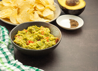 Wall Mural - Fresh guacamole and crispy potato chips on a plate placed on dark brown background with copy space for text. Top view. Concept of traditional Mexican foods and healthy fruits