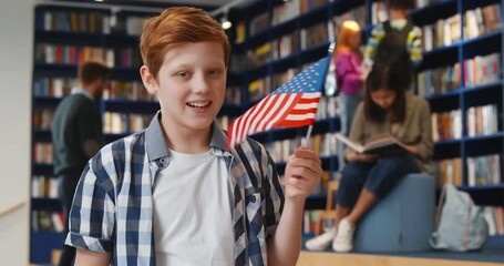 Canvas Print - Portrait of preteen boy holding american flag standing in public school library