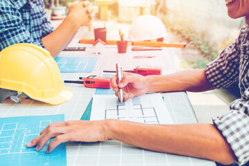 Smiling asia engineer holding pen pointing equipment architects On the desk with a blueprint in the office, Vintage, Sunset light. Concept architects, Selective Focus