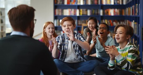 Canvas Print - Multiethnic group of kids sitting on floor near teacher and applauding