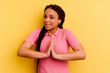 Young african american woman isolated on yellow background holding hands in pray near mouth, feels confident.