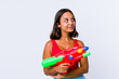 © Asier - Young mixed race woman holding a water gun isolated dreaming of achieving goals and purposes