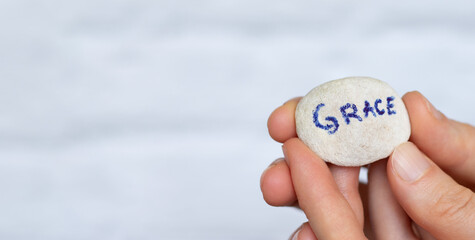 Woman's hand holding stone with handwritten word grace against white background with copy space for text. Biblical concept of God Jesus Christ mercy and love.