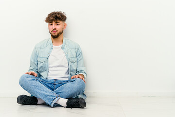 Wall Mural - Young Moroccan man sitting on the floor isolated on white background sad, serious face, feeling miserable and displeased.