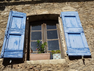 Wall Mural - old light blue wood shutters by an old window on a facade of a stone house with flower pots