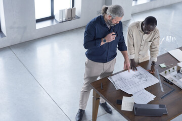 Wall Mural - African young architect examining blueprint of new building together with his partner at the table at office