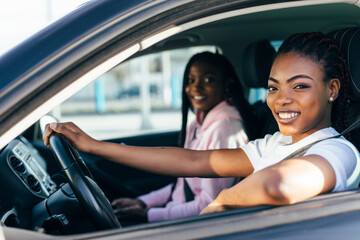 Two african young women on car trip driving the car and making fun.