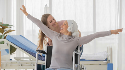 Wall Mural - A middle-aged breast cancer patient on wheelchair and her daughter stretching hands widely with freedom and happiness. Idea for family support and encouragement for sickness members