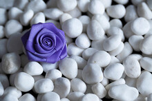 Romantic Background Of White Small Pebbles And Purple Woven Homemade Rose Flower.